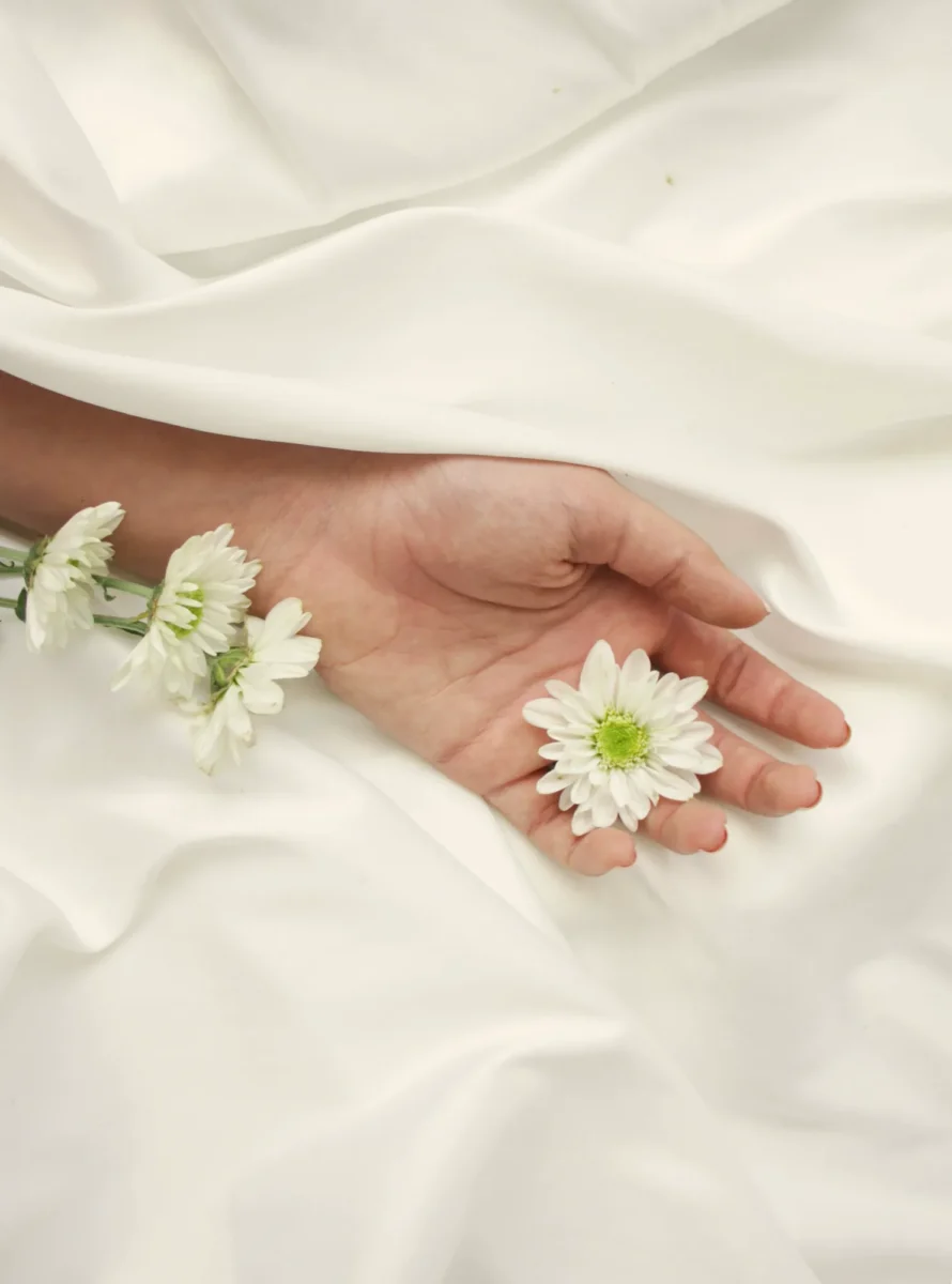 Hand holding white flowers on draped ivory satin