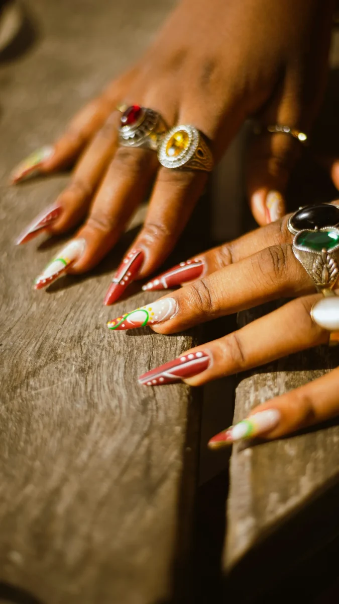 Hands with rings and hand-painted nail art resting on warm wood in sunlight