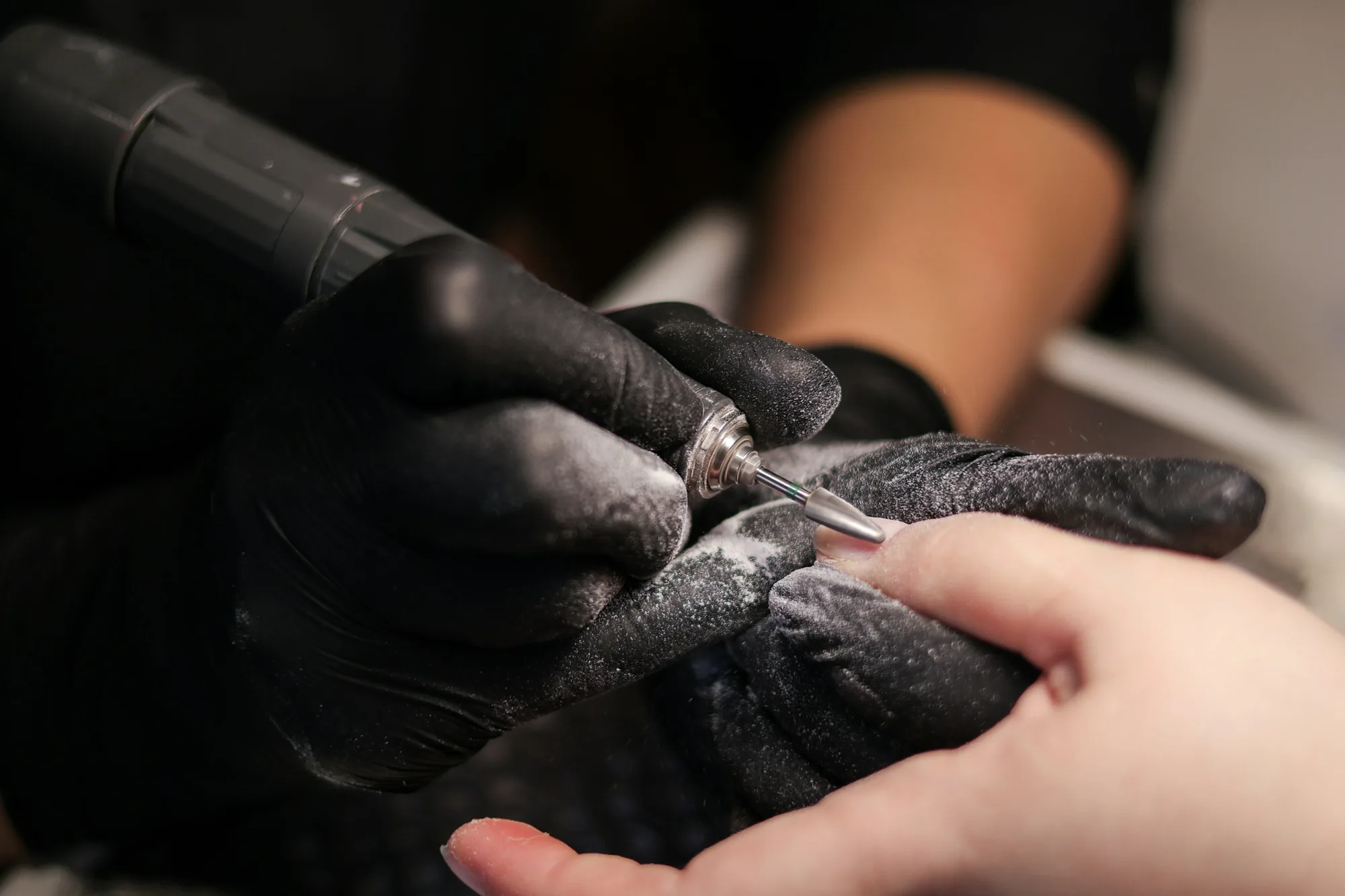 Gloved nail technician using an electric file around a client's cuticle