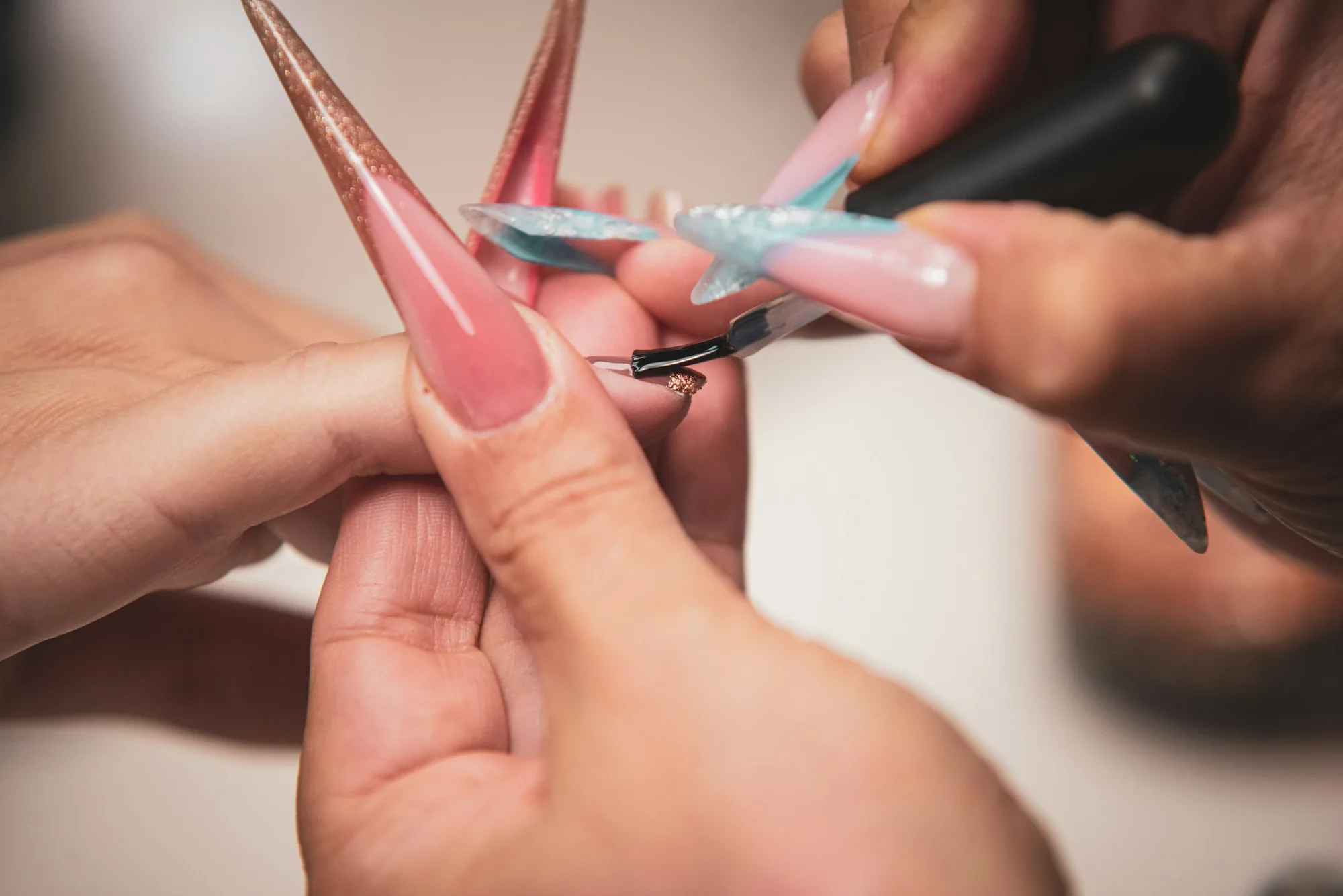 Nail technician sculpting long pink extensions with a fine brush