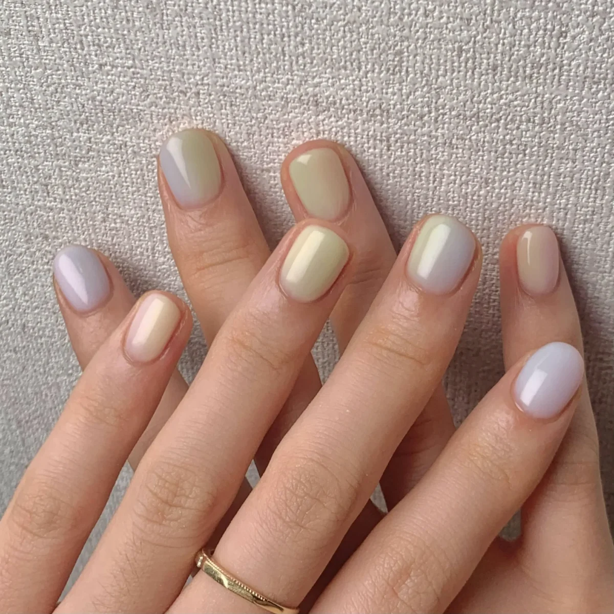 Short natural nails in soft sheer shades resting on beige linen