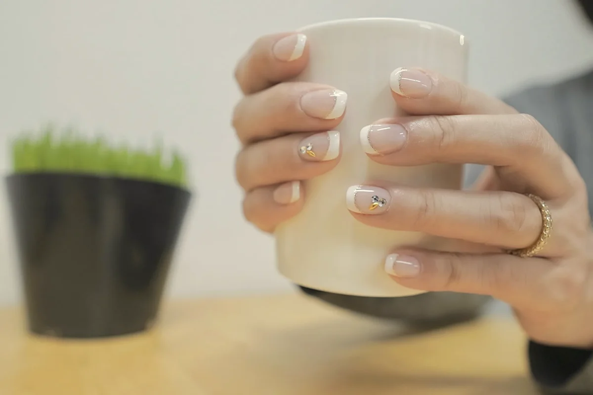 Hands with short nude nails wrapped around a white mug