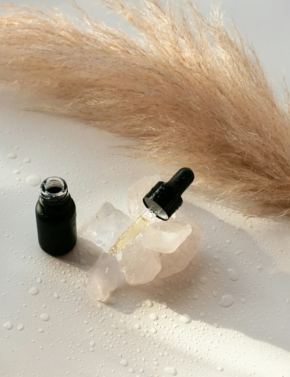 Dropper bottles of oil beside a crystal and dried pampas grass