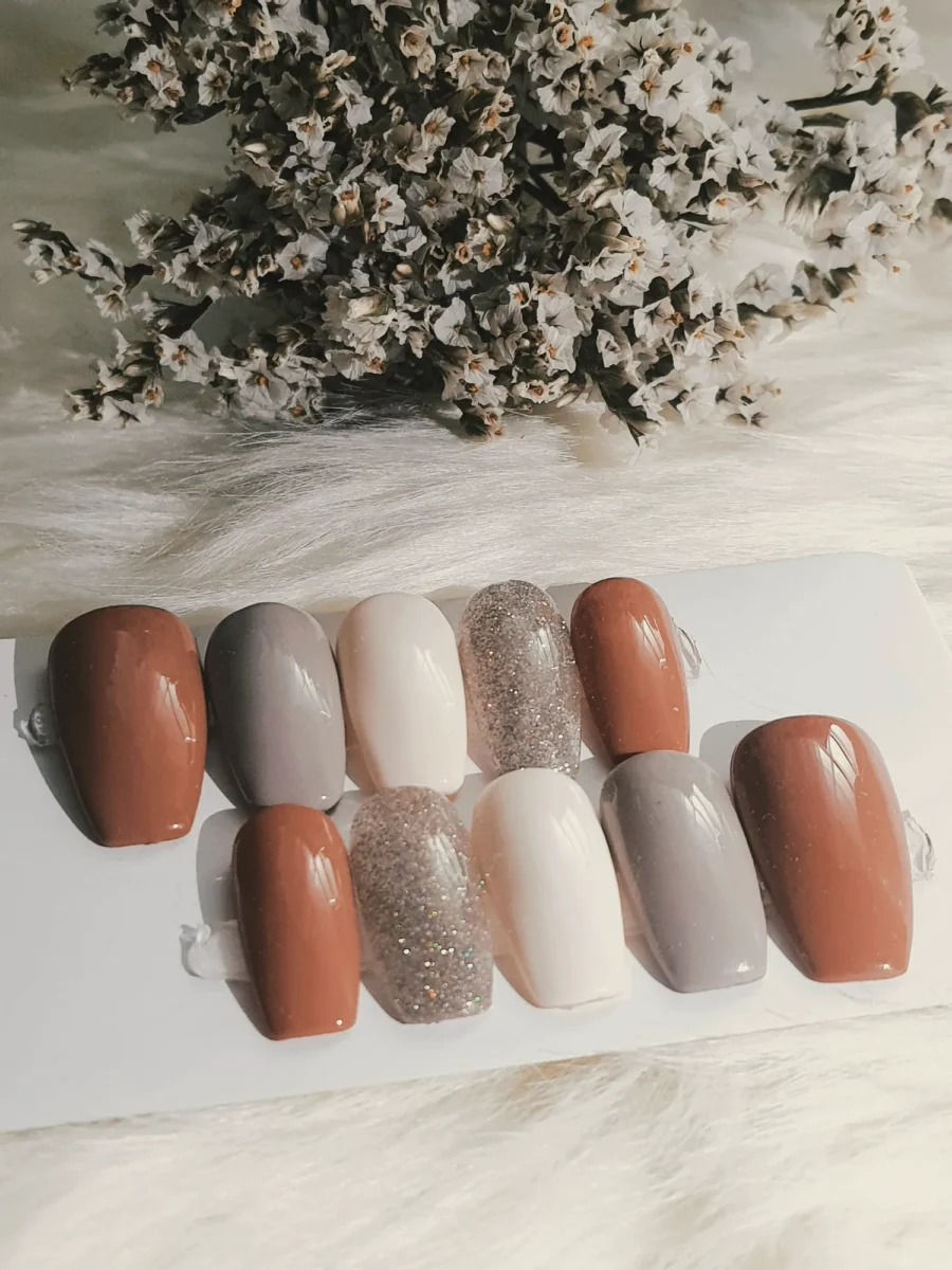 Row of nail tips in nude, caramel, brown and white shades on soft white fur