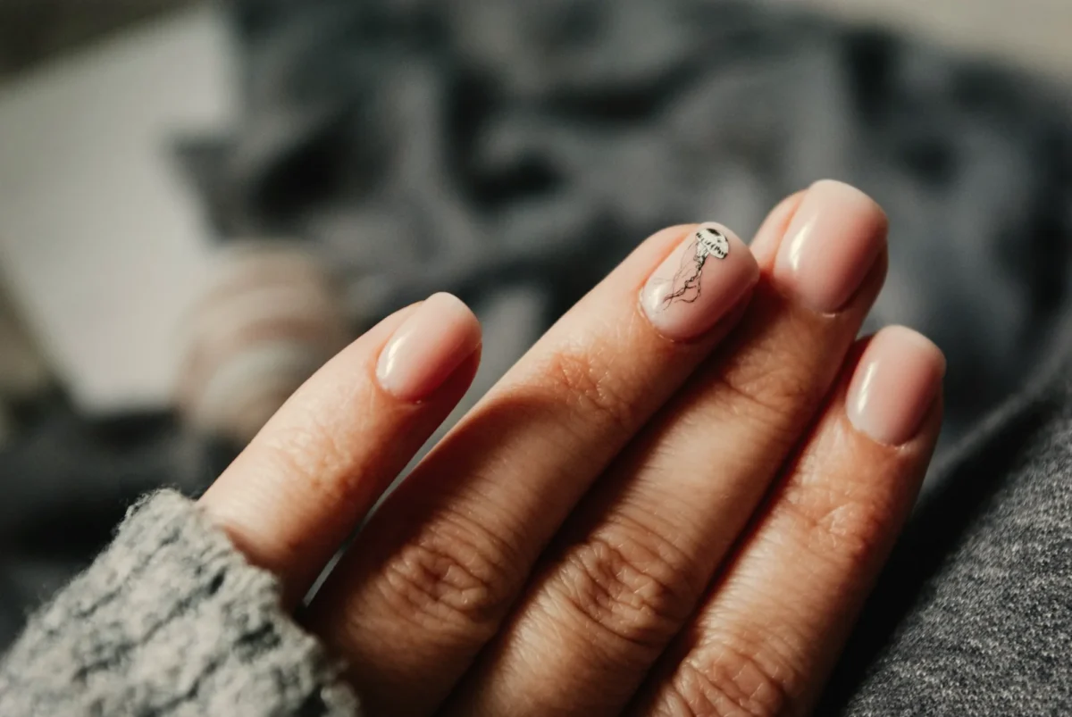 Short glossy nude nails against a grey knit sleeve