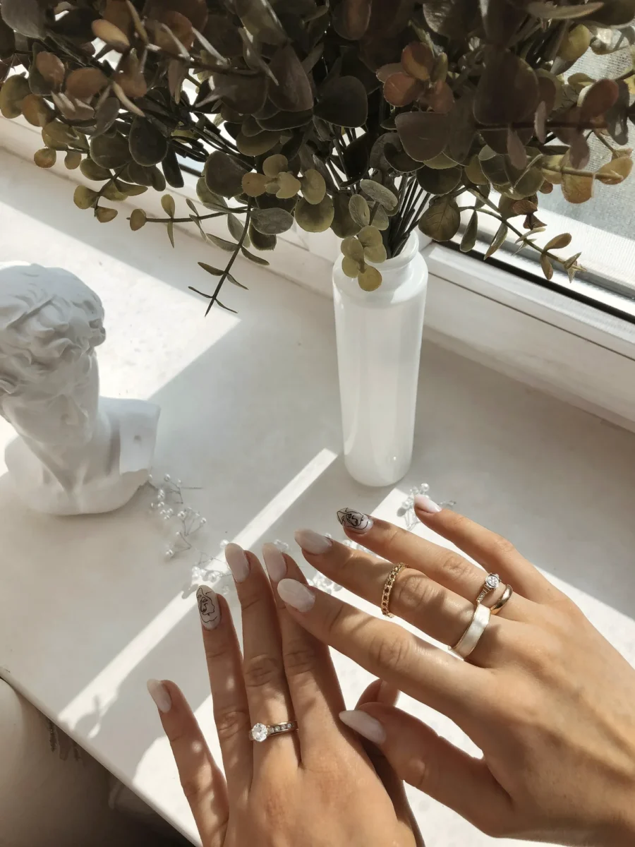 Hands with neutral almond nails and gold rings beside eucalyptus