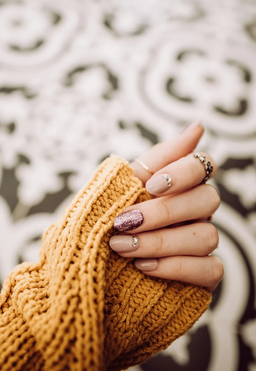 Hand with nude nails and a glitter accent holding the sleeve of a mustard knit sweater