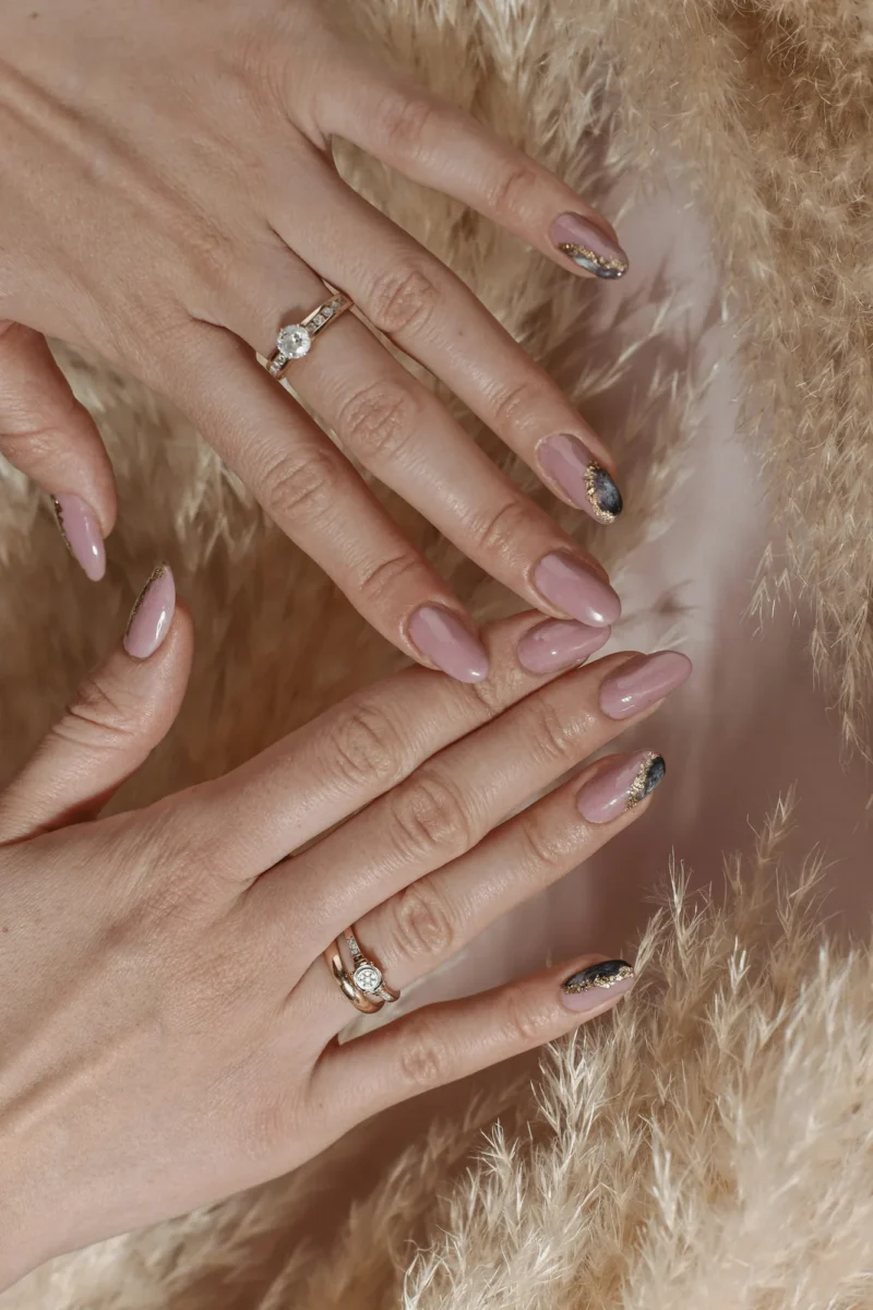 Hands with mauve nude manicured nails and gold rings on dried pampas grass