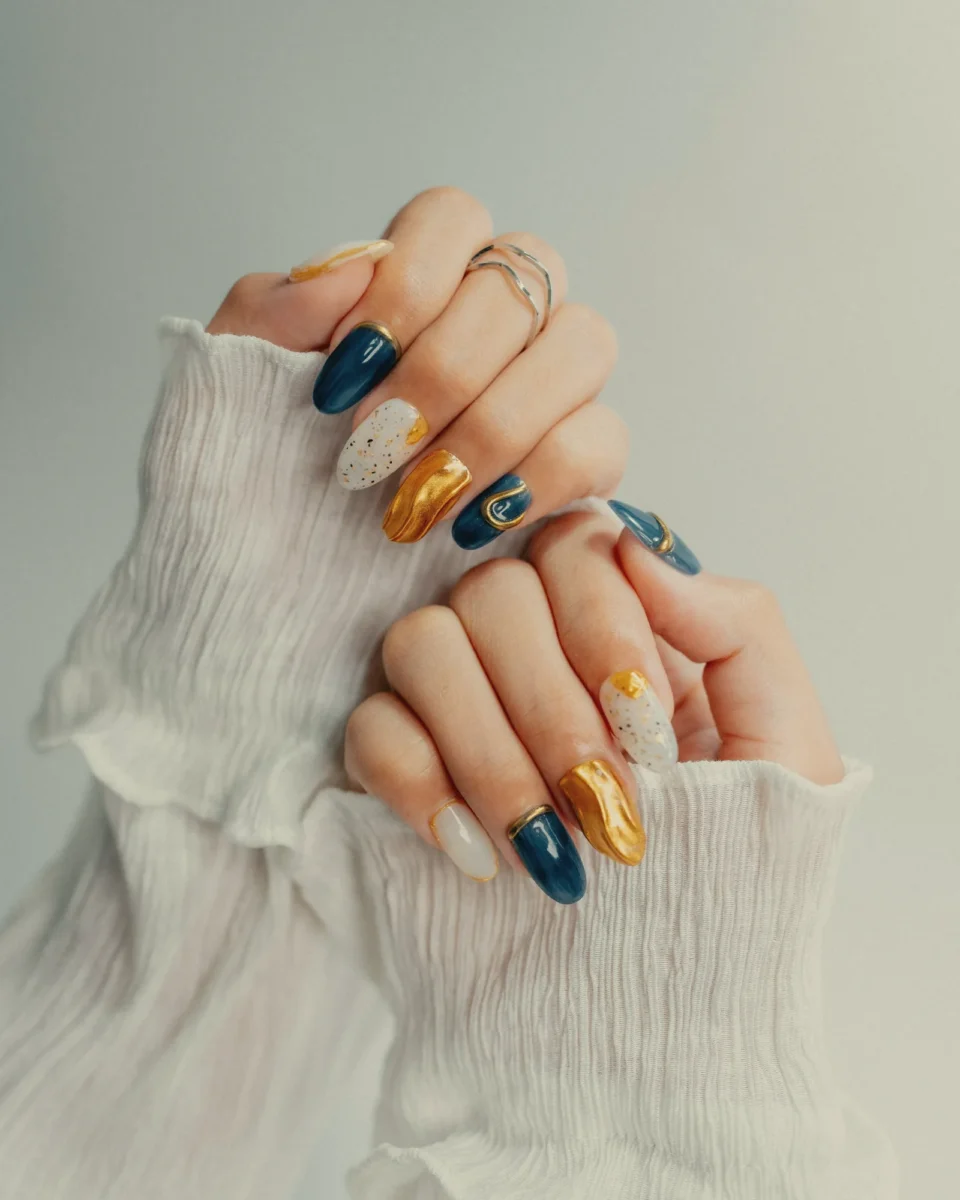 Hands with hand-painted navy, gold and white nail art in white ruffled sleeves