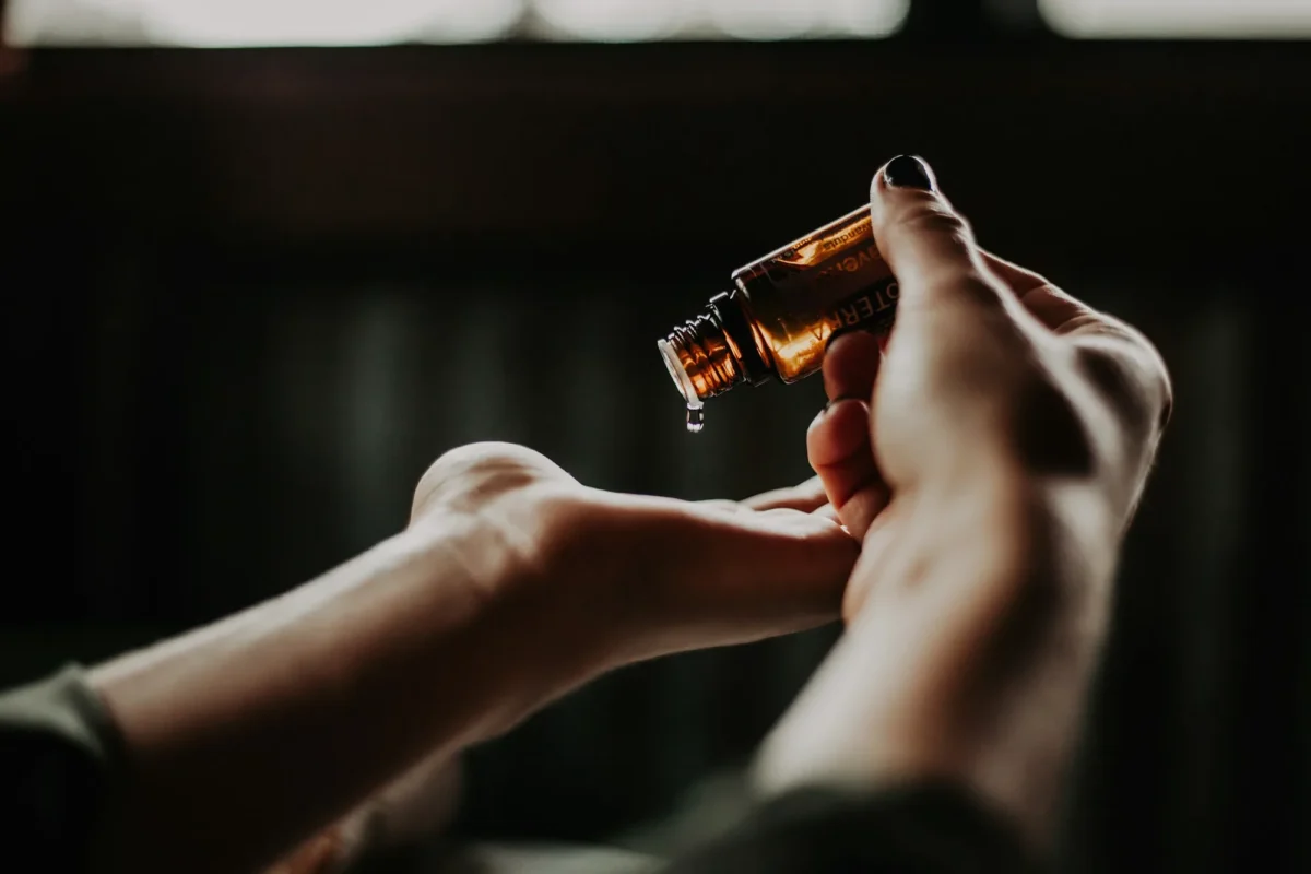 Hands holding an amber dropper bottle of oil in low light