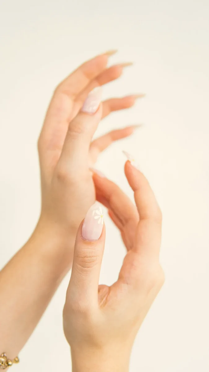 Two hands with clean cuticles and pale nude nails on a white background