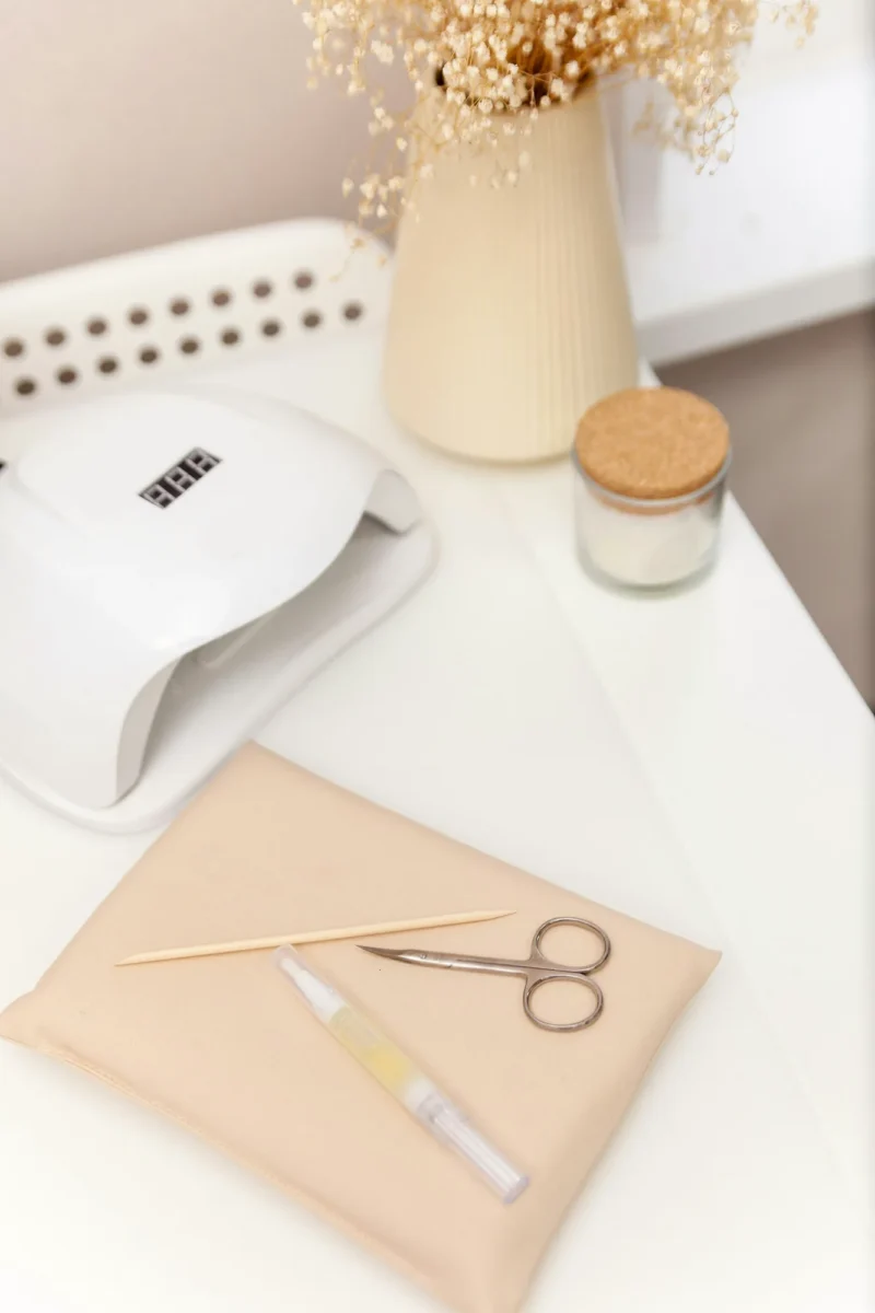 Manicure table with an LED lamp, cuticle scissors and an orange stick on a beige pad beside dried flowers