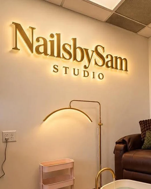 The illuminated gold NailsbySam Studio sign above the brass arc lamp